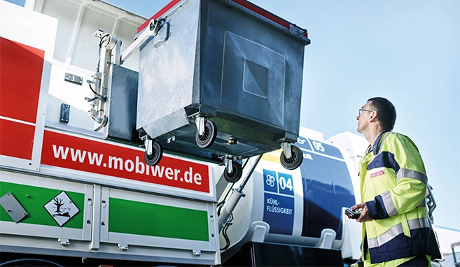 Ein MOBIWER-Fahrer in Warnschutzkleidung steht vor dem MOBIWER und entleert einen Abfallbehälter