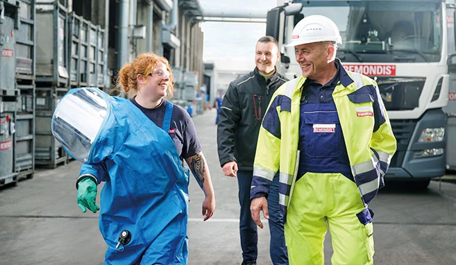 Mitarbeiter mit Warnschutzkleidung und PSA im Recyclingzentrum Bramsche laufen lachend auf die Kamera zu
